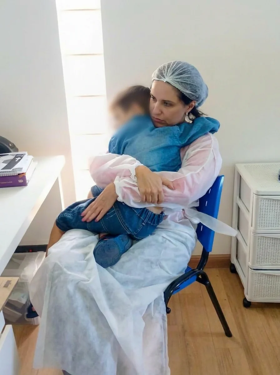 Dra. Roberta, paramentada, acalma um menino adormecido no colo antes do atendimento