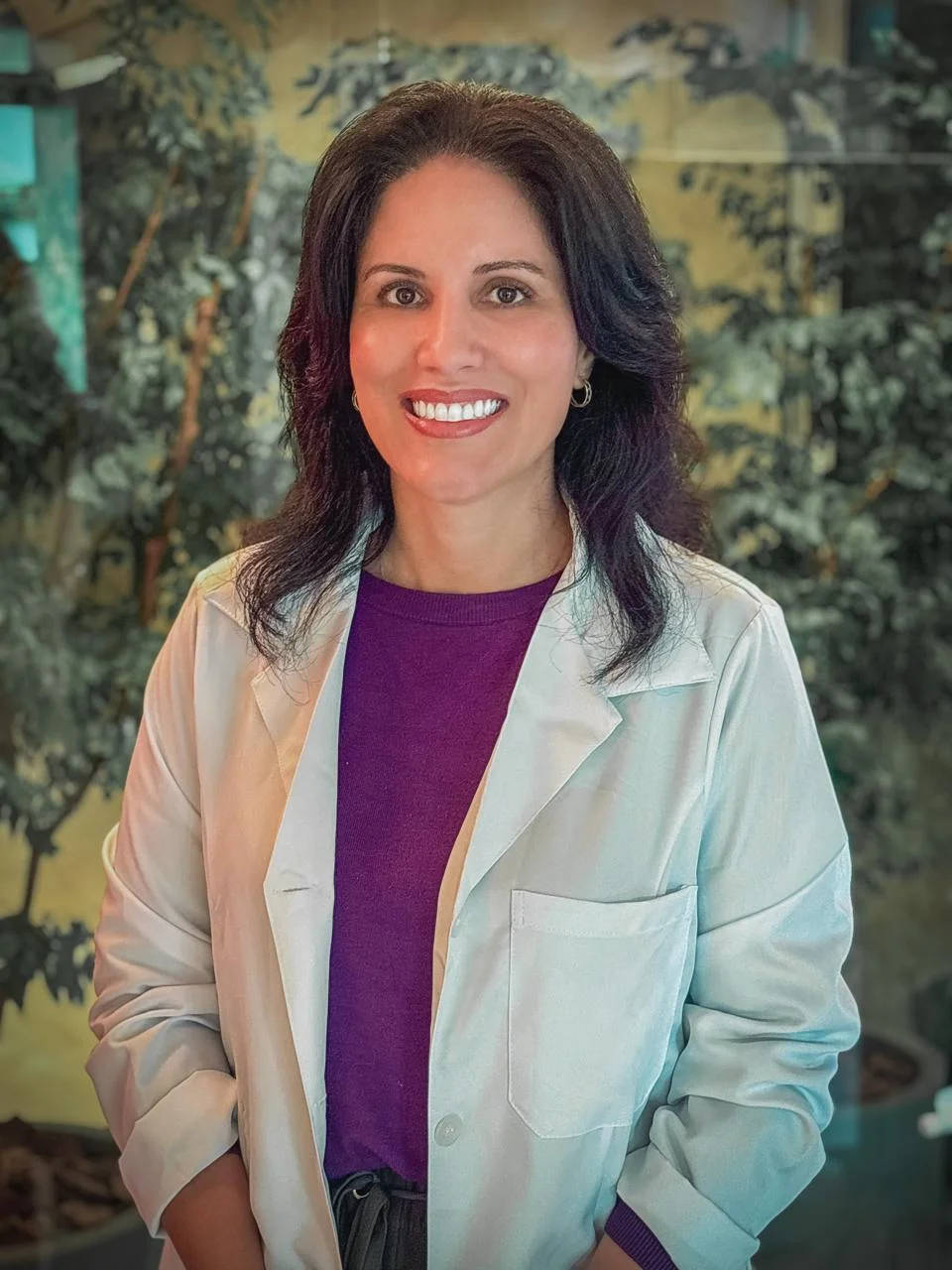 Dra. Roberta de jaleco branco no jardim interno do hospital, sorrindo